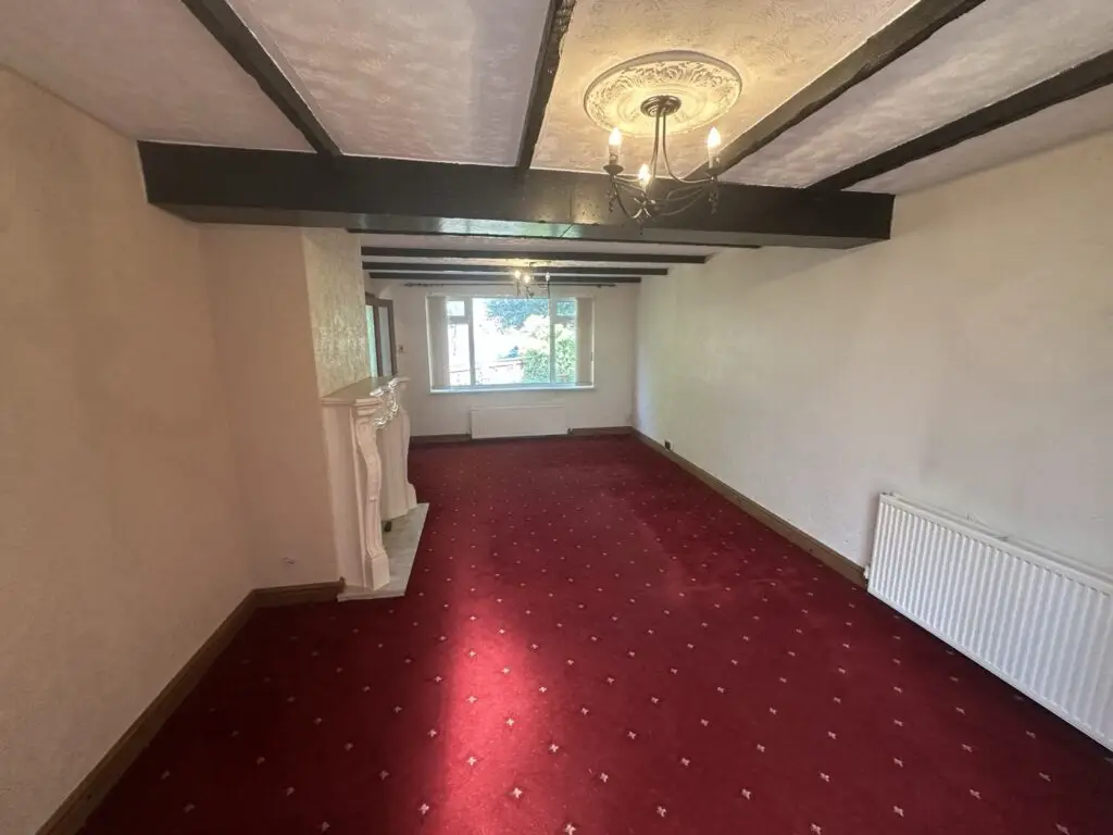 Living room with dated carpet, beams and fire surround before the refurbishment, looking towards the window
